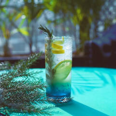 a glass of green to blue liquid with a lemon twist, slice of lime, and sprig of leaves.